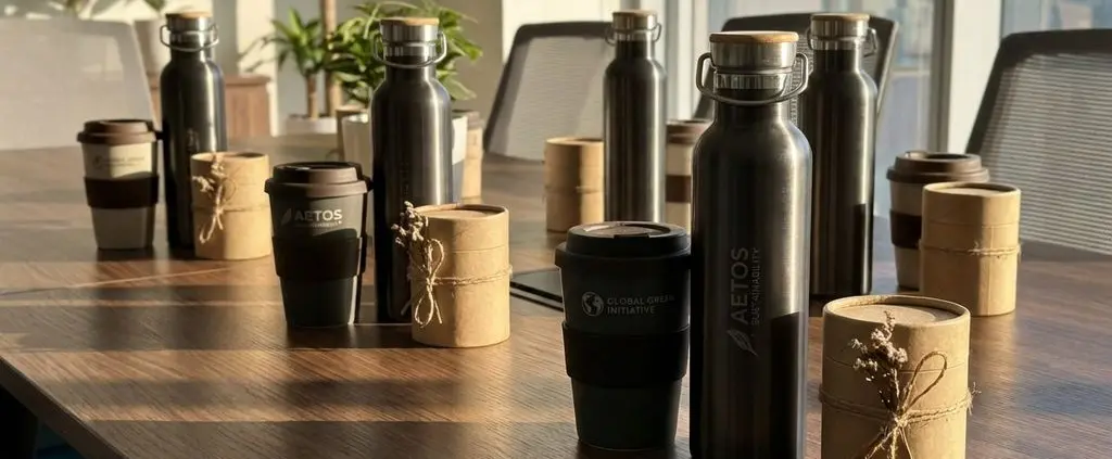 Luxe herbruikbare waterflessen en koffiemokken met gravure op houten vergadertafel met eco-vriendelijke geschenkdozen