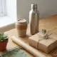 Duurzame relatiegeschenken op houten bureau: RVS waterfles, herbruikbare koffiebeker en eco-vriendelijke verpakking