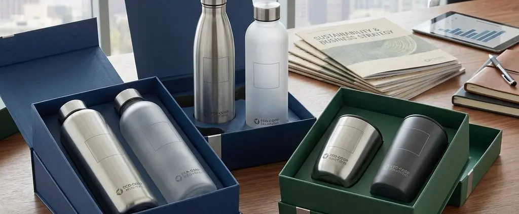 Duurzame waterflessen en koffiemokken als bedrijfscadeaus op houten bureau met elegante verpakking in kantooromgeving