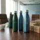 Premium duurzame waterflessen en koffiemokken in groen en blauw op houten bestuurstafel met cadeauverpakking