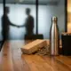Elegante houten bestuurstafel met duurzame relatiegeschenken: RVS waterflessen en thermische koffiemokken in warme tinten