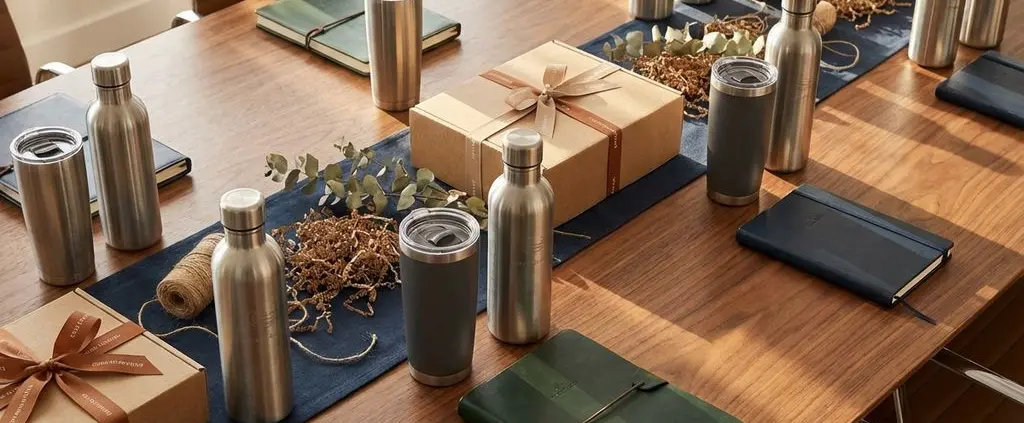 Luxe zakelijke relatiegeschenken op houten vergadertafel: thermobekers, waterfles, notitieboeken met duurzame verpakking