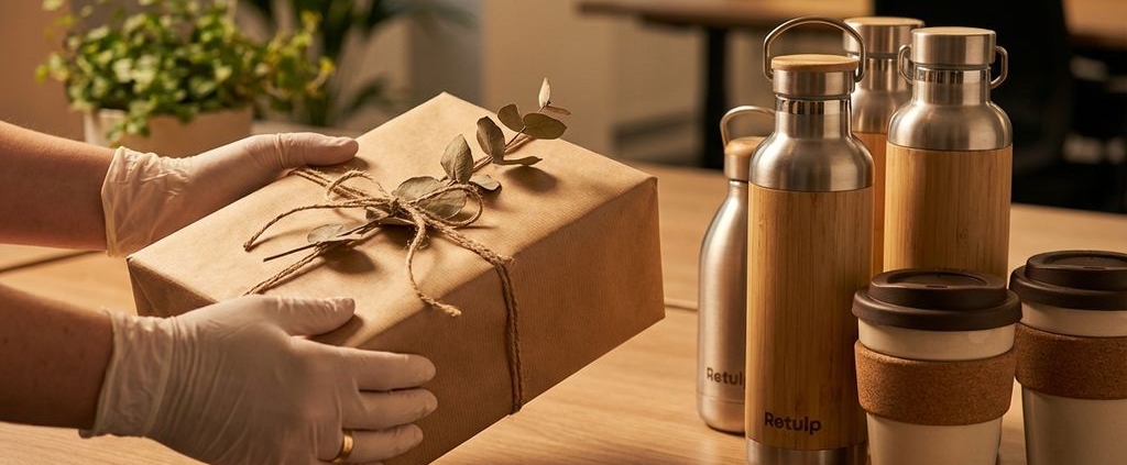 Elegante handen presenteren cadeauverpakking op modern bureau met duurzame herbruikbare flessen en bekers