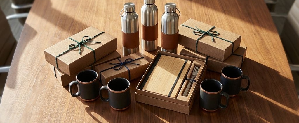 Luxe zakelijke cadeaus op houten vergadertafel: roestvrijstalen waterflessen, koffiemokken en duurzame geschenkdozen