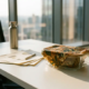 Bijenwasdoek over glazen lunchcontainer op wit kantoorbureau met documenten en herbruikbare waterfles op achtergrond