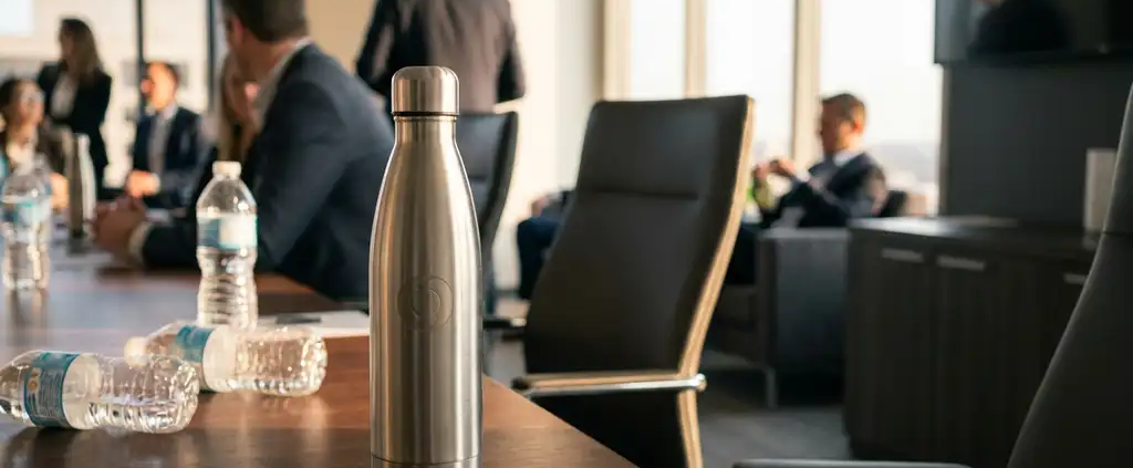 Stalen herbruikbare waterfles op conferentietafel omringd door wegwerp plastic flessen in kantooromgeving