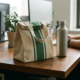 Canvas lunchtas en roestvrijstalen waterfles op houten bureau in modern kantoor met natuurlijk licht