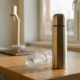 RVS thermosfles met geborstelde afwerking naast wegwerpbare plastic fles op modern bureau, warme natuurlijke verlichting