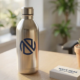 Roestvrijstalen waterfles met marineblauw bedrijfslogo op houten bureau naast visitekaartjes en vetplant