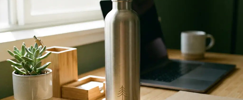 Roestvrijstalen waterfles met bedrijfslogo op modern bureau omringd door bamboe kantoorbenodigdheden en vetplant