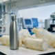 Roestvrijstalen waterfles met matte afwerking op laboratoriumtafel, omringd door gebarsten plastic flessen en wetenschappelijke apparatuur