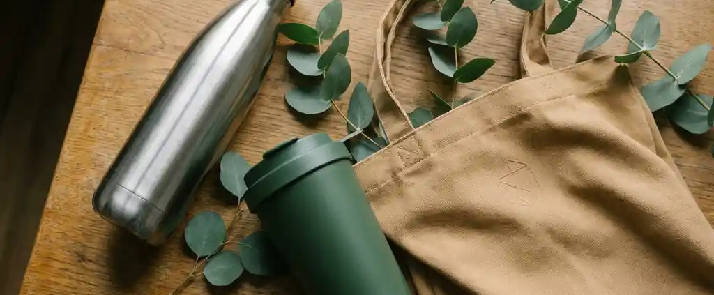 Duurzame relatiegeschenken: roestvrijstalen drinkfles, matte thermobeker en branded tote bag op eiken bureau met eucalyptustakjes.