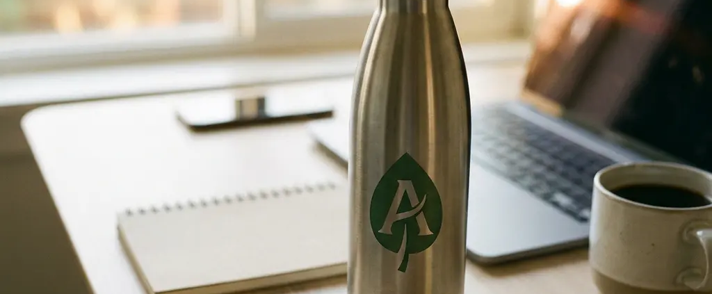 Gepersonaliseerde roestvrijstalen herbruikbare waterfles op modern bureau met laptop en koffie op de achtergrond.