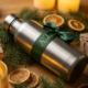 Matte roestvrijstalen drinkfles met gepersonaliseerde strik tussen dennentakken en houten cadeaudozen in warm kaarslicht.