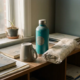 Ongebruikte promotionele items op een rommelig kantoorplank: herbruikbare waterfles, omgekeerde koffiemok en ingepakte tote bag.