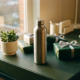 Roestvrij stalen waterfles op modern bureau met ingepakte cadeaus, succulent en warm natuurlijk zijlicht.